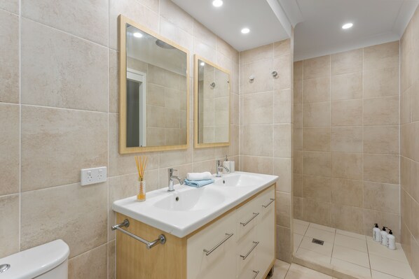 A modern bathroom with a dual sink vanity, a toilet, and a shower area.