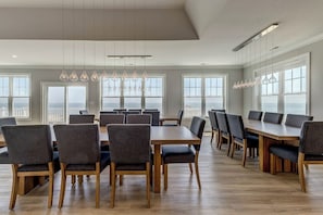 Un vaste espace dédié à la salle à manger, avec de nombreuses tables et chaises, de grandes fenêtres offrant une vue dégagée et un éclairage suspendu.