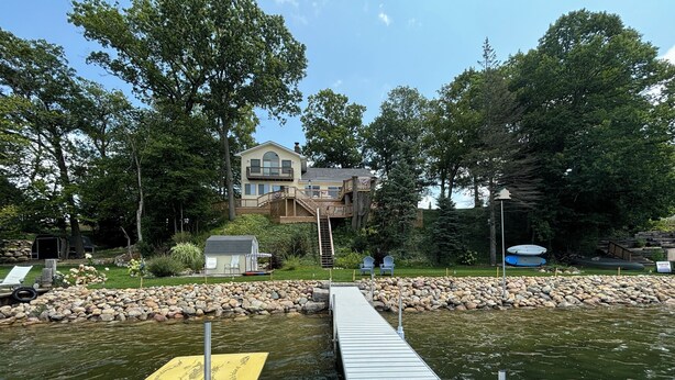 A dock leading to a house with a deck and a small shed. - Private Dock on Pine Lake – Sleeps 15 – Family Lakefront Retreat (Plainwell)