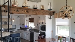 A spacious kitchen with wooden beams, a dining area with a wooden table, and a staircase with a cat tree. - Private Dock on Pine Lake – Sleeps 15 – Family Lakefront Retreat (Plainwell)