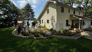 A two-story house with a covered porch and a stone fireplace. - Private Dock on Pine Lake – Sleeps 15 – Family Lakefront Retreat (Plainwell)