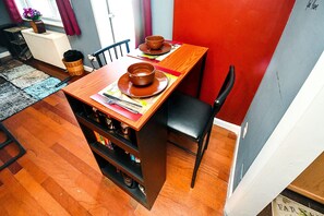 A compact dining area with a wooden table set for two, a black chair, and a small kitchen area with shelves. - FIFA 1BR Dtwn ATL-Skyline Balcony | 1mi to Stadium (Atlanta)
