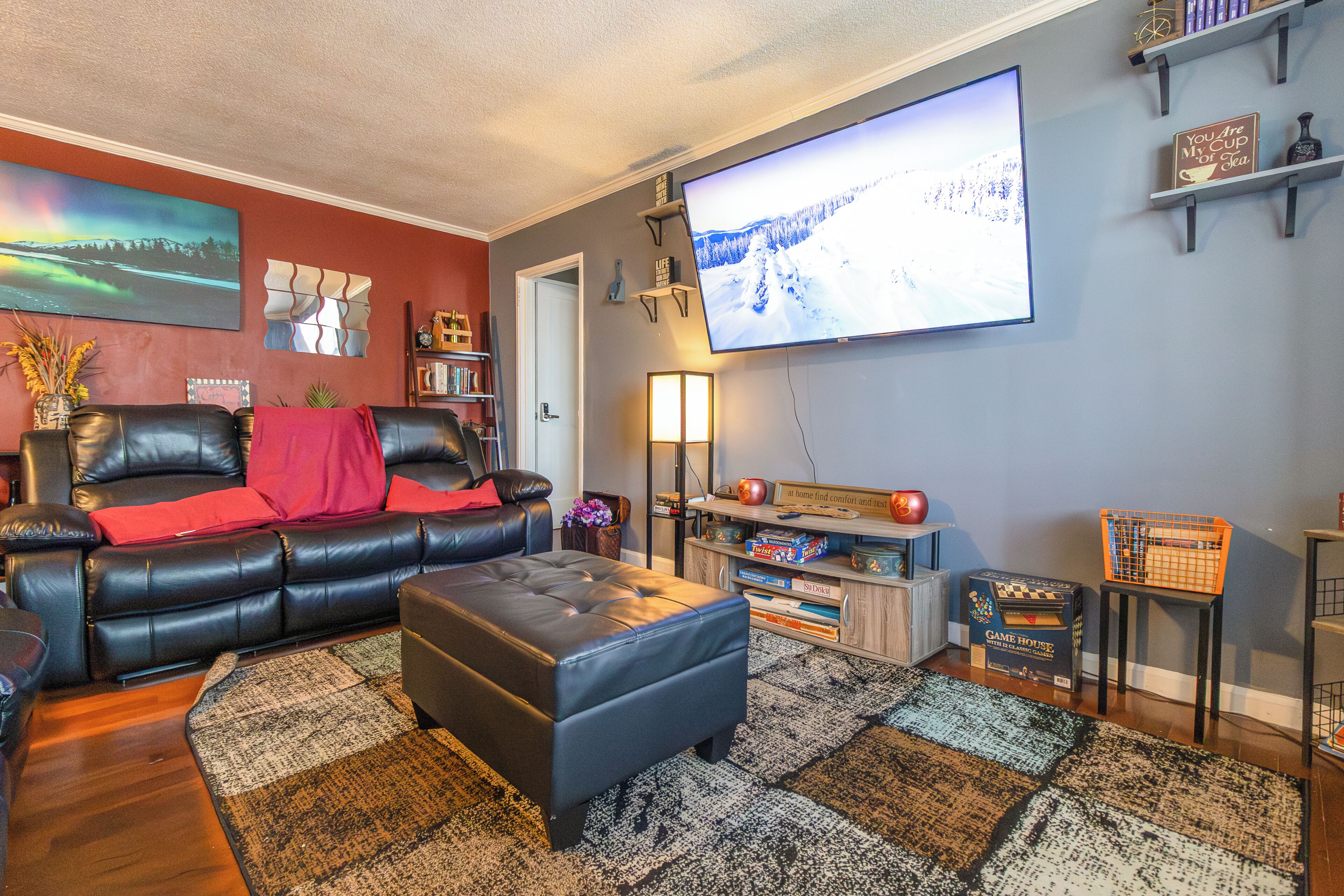 A living room with a black leather sofa, a large flat-screen TV, a wooden coffee table, and a bookshelf.