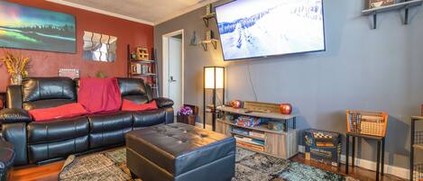 A living room with a black leather sofa, a large flat-screen TV, a wooden coffee table, and a bookshelf.