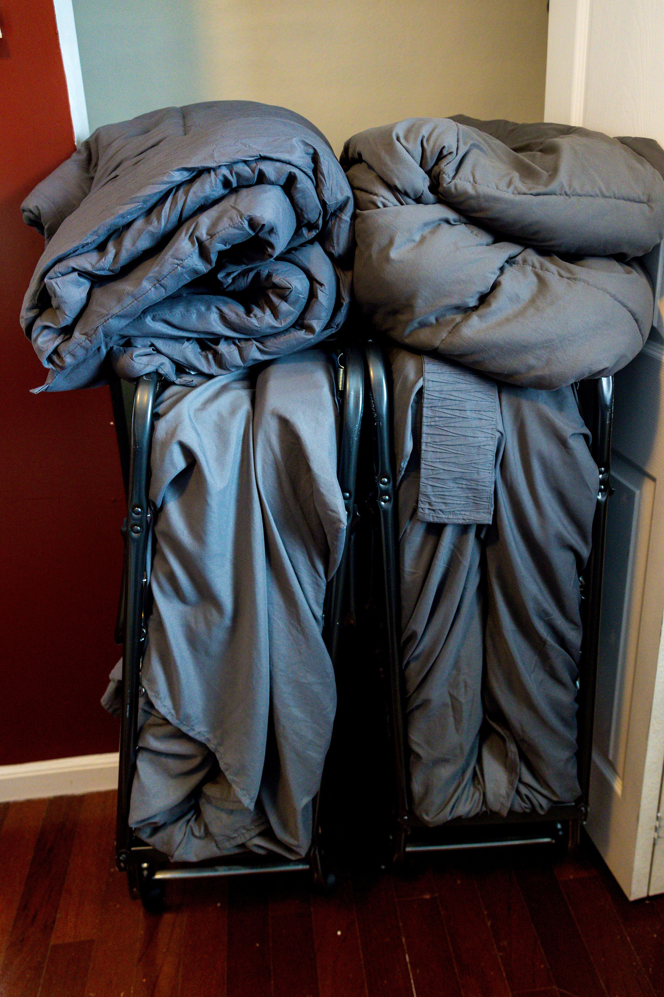 A stack of gray bedding on a metal rack in a room with wooden flooring and a red wall.