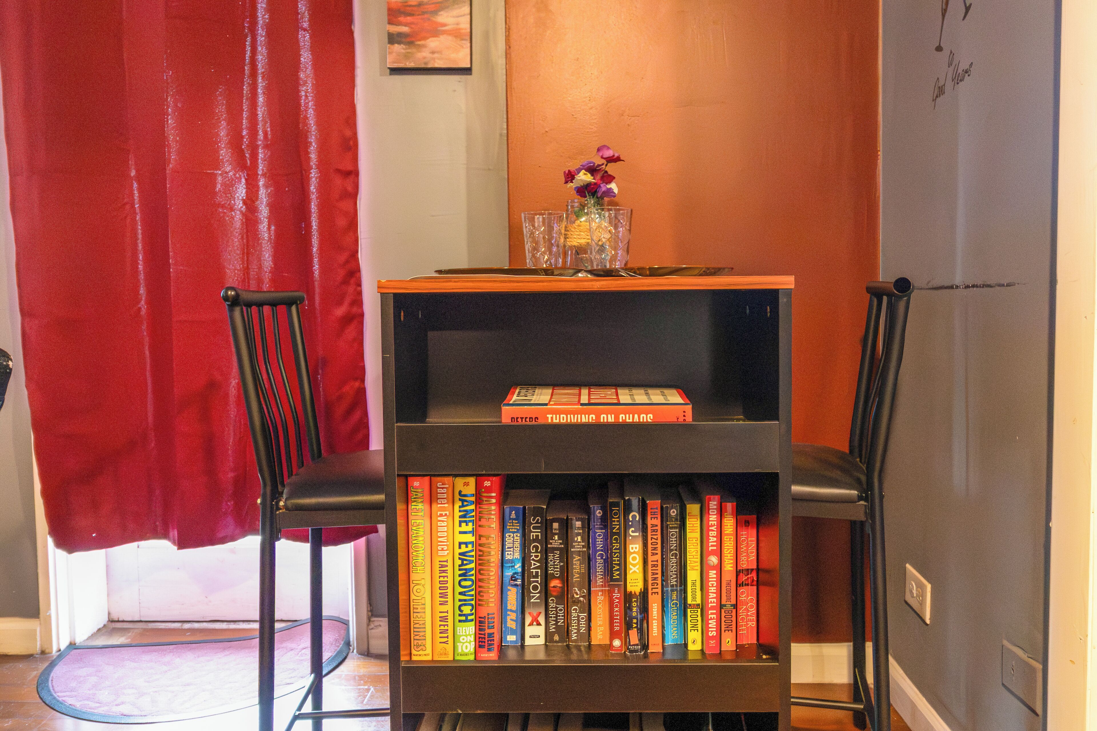 A bookshelf with books, a vase with flowers, and two chairs.