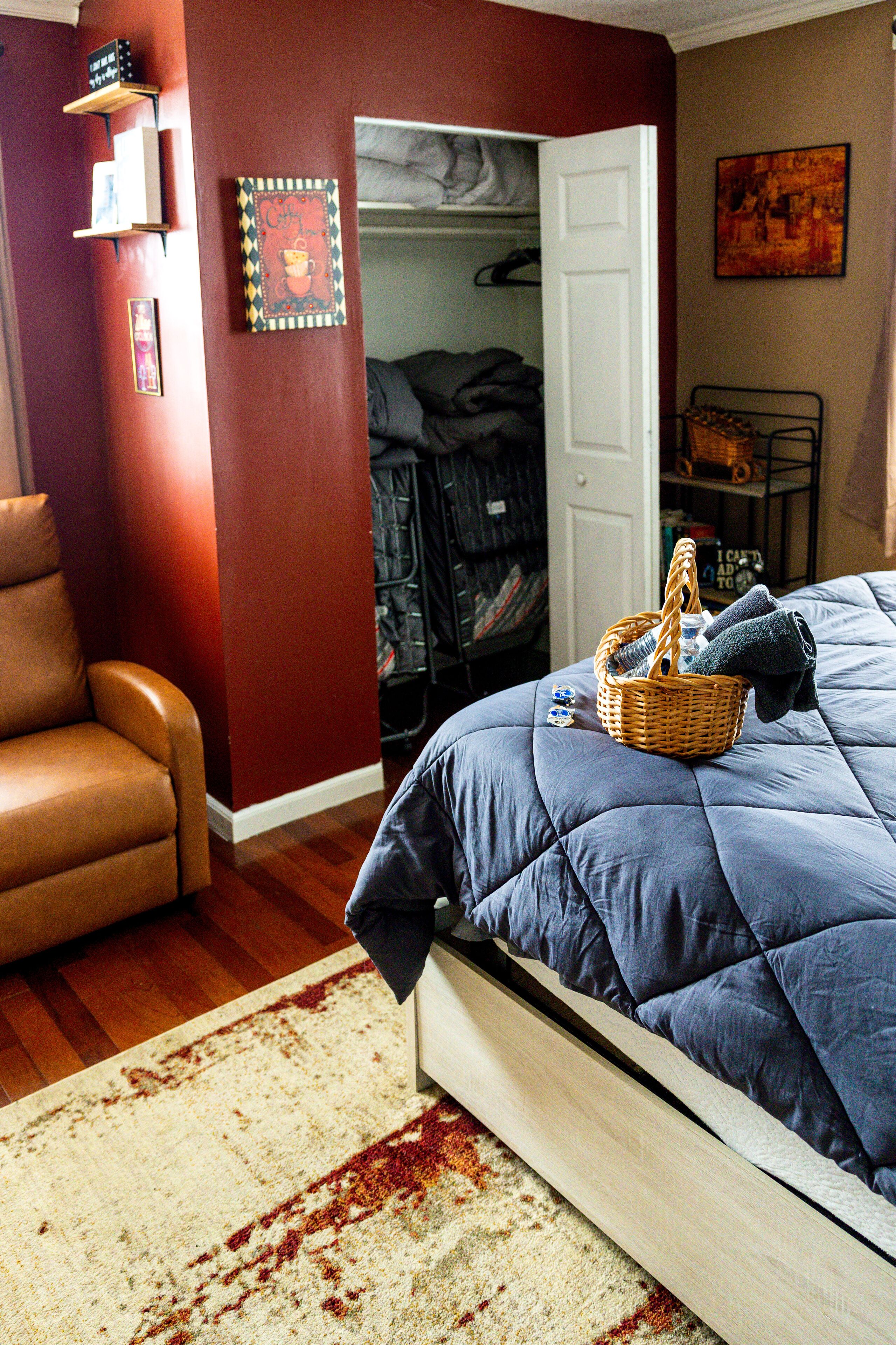 A bedroom with a bed, a chair, a closet, and a door leading to another room.