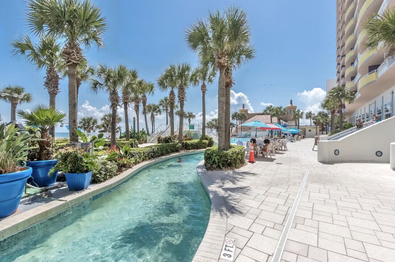 A poolside area with palm trees, a clear pool, and a tiled walkway.