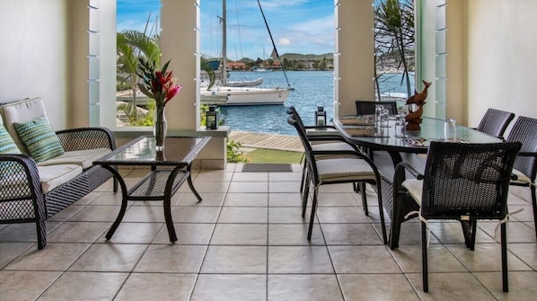 A patio with a glass table and chairs, a view of a marina with boats, and a tropical plant arrangement. - Marina-view 3BR condo in Rodney Bay with pool, AC & WiFi, Harbour#7 (Rodney Bay)