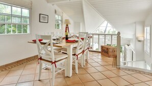 A dining area with white furniture, red ribbons, and a view of greenery outside. - Beautiful 2-bed cliffside villa - Saline Reef (Cap Estate)
