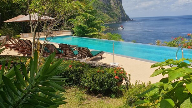 Un espace piscine avec des chaises longues, une vue dégagée sur l’océan et un paysage montagneux en toile de fond.