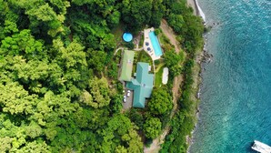 Vue aérienne d’une propriété située sur la côte, avec une piscine, un patio couvert et un quai pour bateaux.