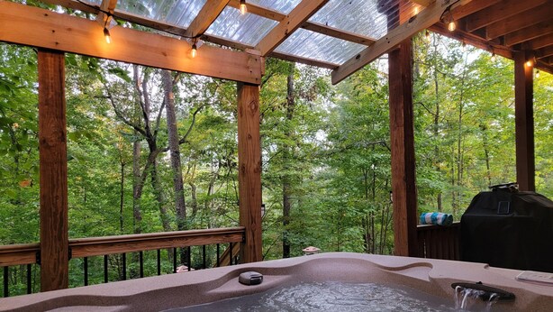 A hot tub with a wooden deck and glass ceiling, surrounded by a forest. - Relaxing Helen, Ga Cabin Min from Helen, Sleeps 12 with Hot Tub & Firepit! 
     (Sautee Nacoochee)