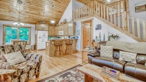 A spacious living area with a wooden ceiling, a kitchen with a bar, a leather sofa, and a staircase. - Relaxing Helen, Ga Cabin Min from Helen, Sleeps 12 with Hot Tub & Firepit! 
     (Sautee Nacoochee)