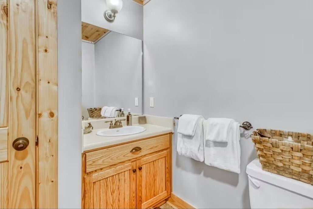 Un baño con tocador de madera, un lavabo blanco y un inodoro con una cesta de mimbre.