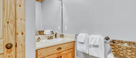 Un baño con tocador de madera, un lavabo blanco y un inodoro con una cesta de mimbre.