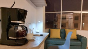 A modern living space with a coffee maker on a wooden table, a teal sofa with yellow cushions, and a window with a view of the city at night. - HOTEL LIBERTAD 109  (La Libertad)