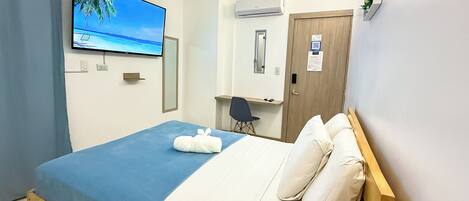 Habitación de hotel con cama, escritorio, silla, televisión, aire acondicionado y puerta.
