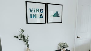 En hall med ett mörkt trägolv, en vit dörr och ett svart konsolbord med två vaser och en liten växt. Två inramade tavlor hänger på väggen ovanför bordet.