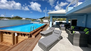 A poolside area with a wooden deck, lounge chairs, and a covered seating area with cushions. - Spacious Waterfront Sanctuary (Jolly Harbour)