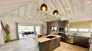 A modern kitchen with an island, built-in appliances, and a dining area with a view. - Spacious Waterfront Sanctuary (Jolly Harbour)