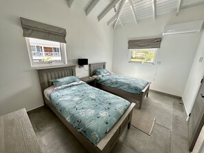 A bedroom with two beds, a TV, and a window with a view of greenery. - Spacious Waterfront Sanctuary (Jolly Harbour)