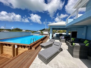 A poolside area with a wooden deck, lounge chairs, and a covered seating area with cushions. - Spacious Waterfront Sanctuary (Jolly Harbour)