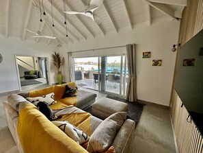 A modern living room with a sofa, a coffee table, and a view of an outdoor balcony. - Spacious Waterfront Sanctuary (Jolly Harbour)