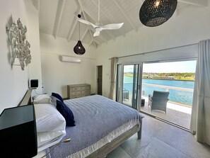 A bedroom with a bed, a ceiling fan, and a view of a body of water through a sliding glass door. - Spacious Waterfront Sanctuary (Jolly Harbour)