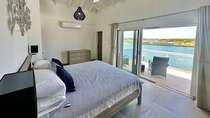 A bedroom with a bed, a ceiling fan, and a view of a body of water through a sliding glass door. - Spacious Waterfront Sanctuary (Jolly Harbour)