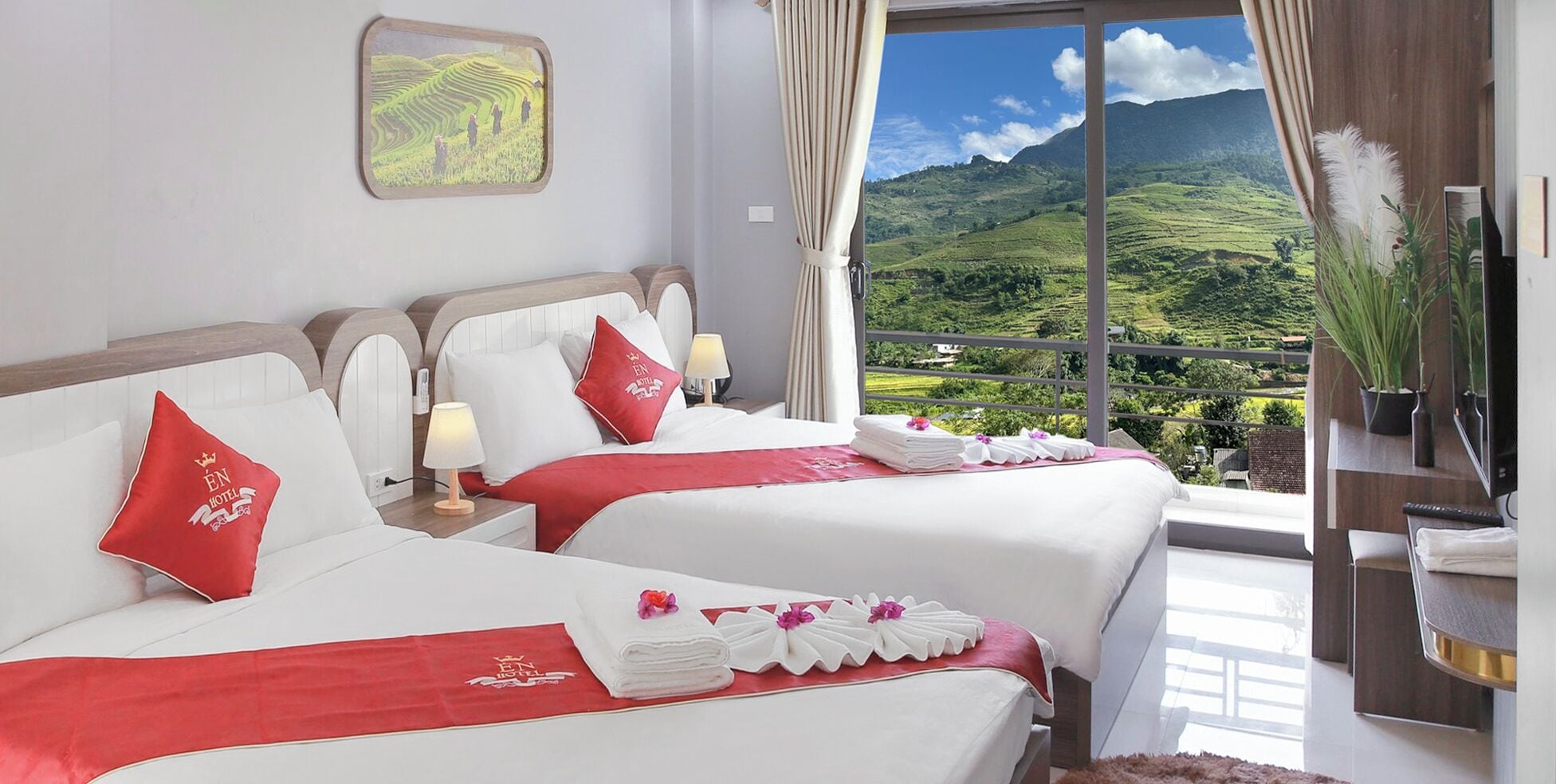 Een hotelkamer met twee bedden, een groot raam met uitzicht op groene heuvels, een televisie en een kleine plant op een plank.