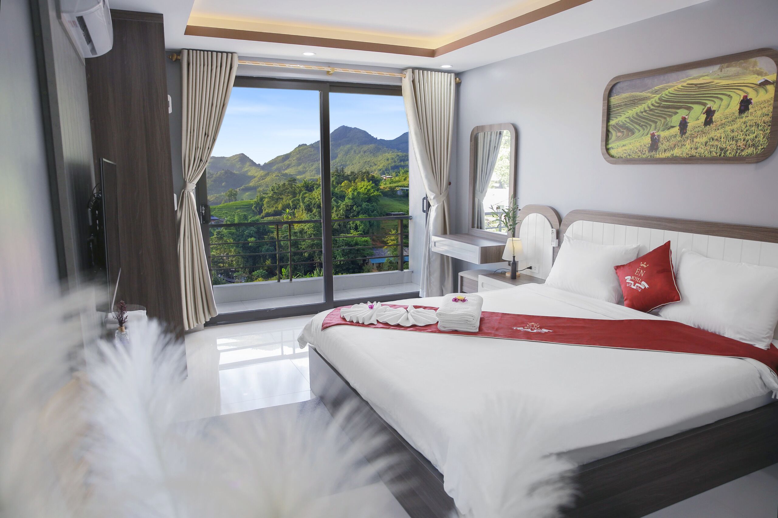 A hotel room with a large bed, a nightstand, a mirror, and a view of a mountainous landscape.