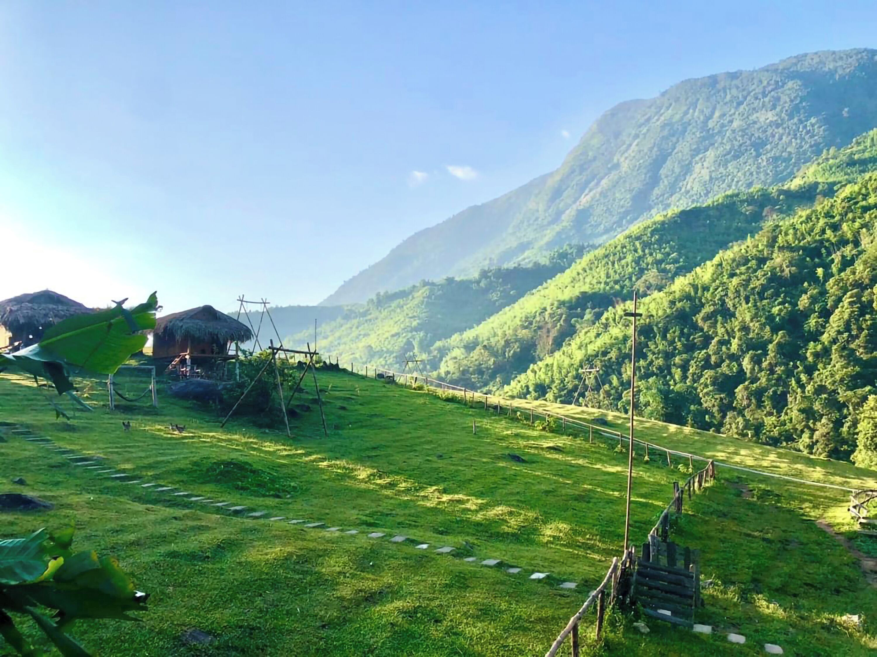 A rural landscape with a thatched-roof hut, a green field, and a mountain in the background.