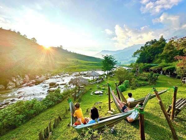 A hammock in a lush green landscape with a river and mountains in the background. - En Hotel Sapa (Ta Van)