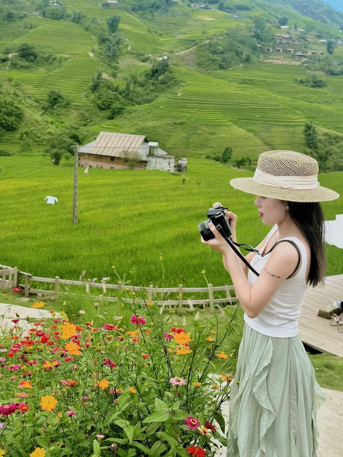 Une femme prend une photo avec un appareil photo dans un cadre rural, avec des champs verdoyants et une clôture en bois.