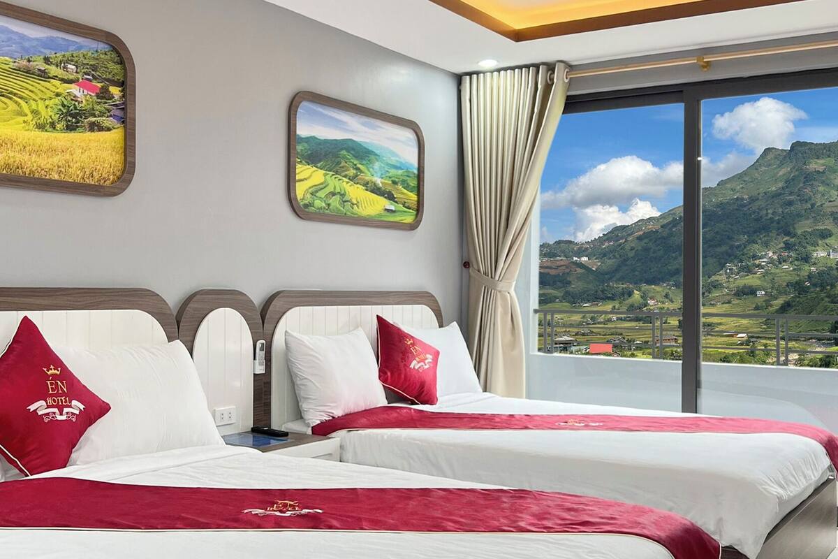 A hotel room with two beds, a large window with a mountain view, and artwork on the walls.