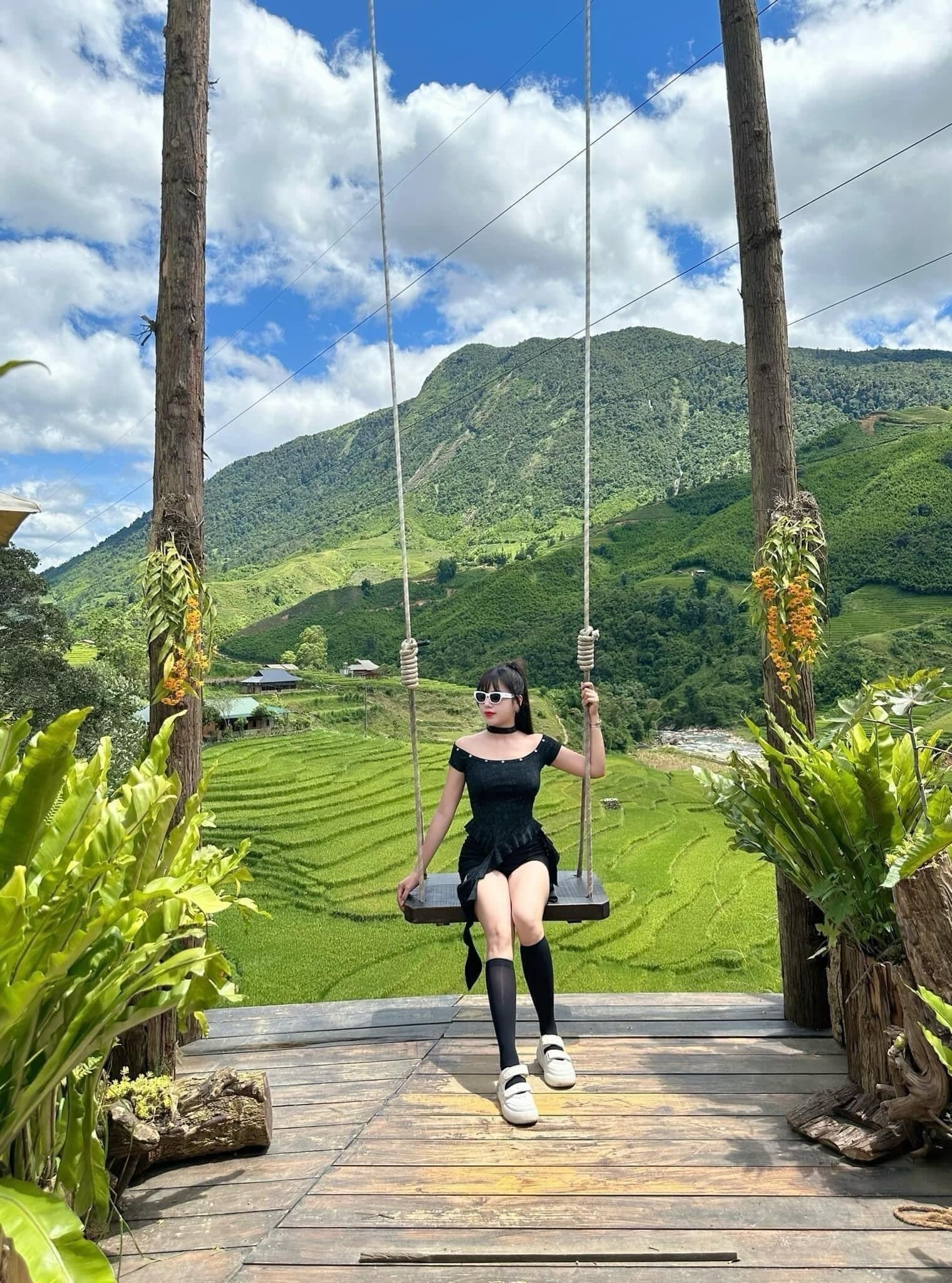 Uma pessoa em um balanço apreciando uma paisagem verdejante com campos em socalcos e colinas ao fundo.