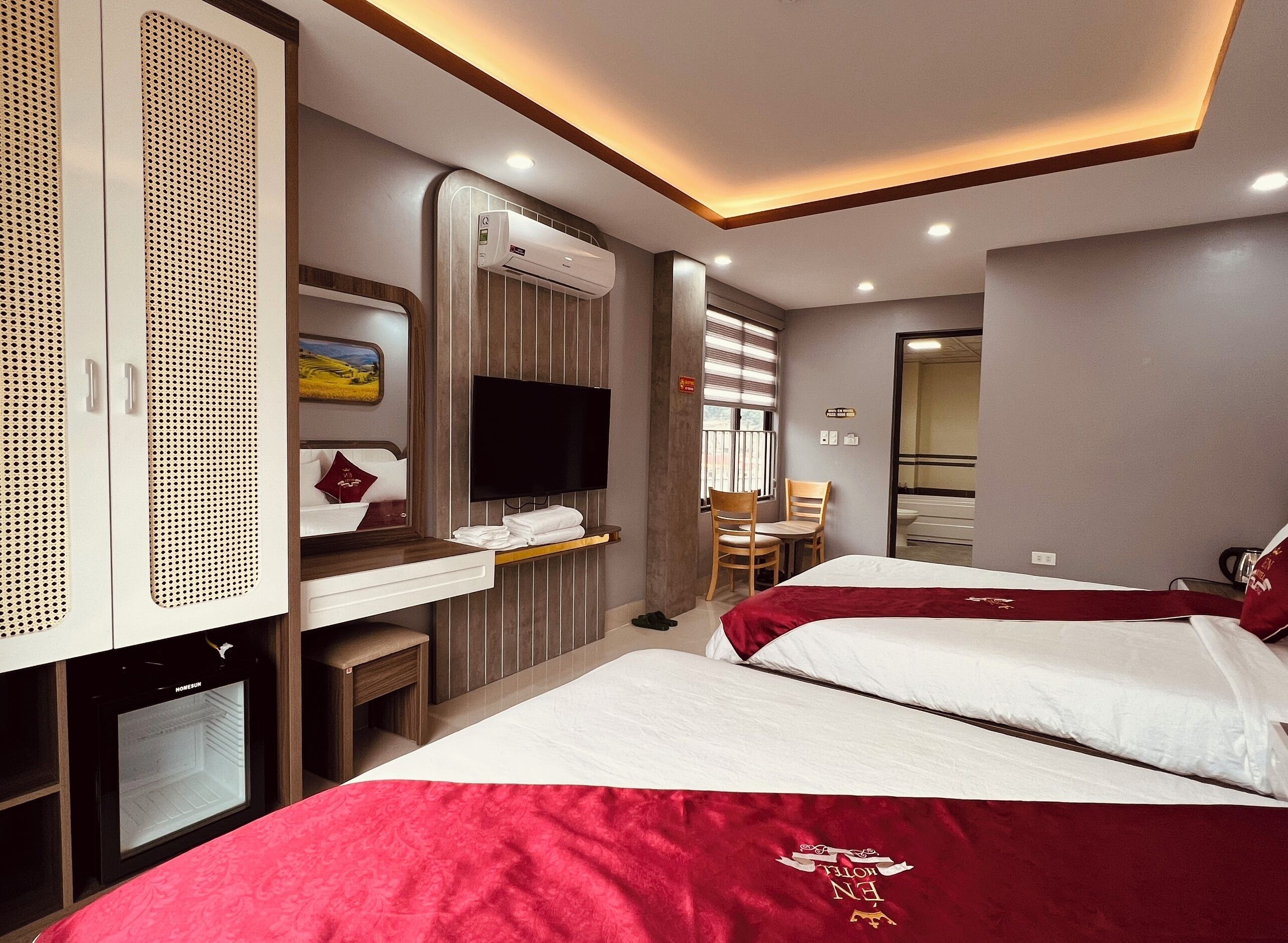 A hotel room with two beds, a TV, a minibar, and a desk with a chair.