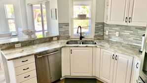 A kitchen with white cabinets, a granite countertop, a stainless steel dishwasher, and a window with a view of greenery. - RENOVATED HOUSE-NEW HEATED POOL-HOT TUB-CLOSE TO BEACH- MACKLE PARK-BEACH GEAR (Marco Island)
