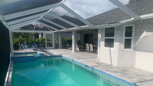 A swimming pool with a covered patio area, lounge chairs, and a view of the surrounding landscape. - RENOVATED HOUSE-NEW HEATED POOL-HOT TUB-CLOSE TO BEACH- MACKLE PARK-BEACH GEAR (Marco Island)