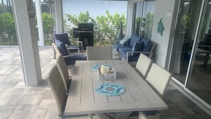 An outdoor patio with a wooden table, wicker chairs, and a blue sofa. - RENOVATED HOUSE-NEW HEATED POOL-HOT TUB-CLOSE TO BEACH- MACKLE PARK-BEACH GEAR (Marco Island)