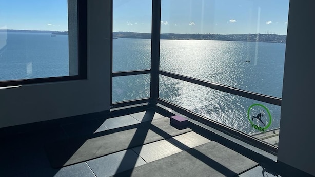 Une pièce dotée de grandes fenêtres donnant sur un plan d’eau, un tapis de yoga et une petite boîte posée sur le sol.