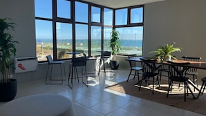 Une pièce spacieuse avec de grandes fenêtres, un coin repas avec des chaises et une table, et des plantes en pot.
