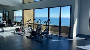 Une salle de sport équipée de matériel d’exercice et dotée de grandes fenêtres donnant sur l’océan.