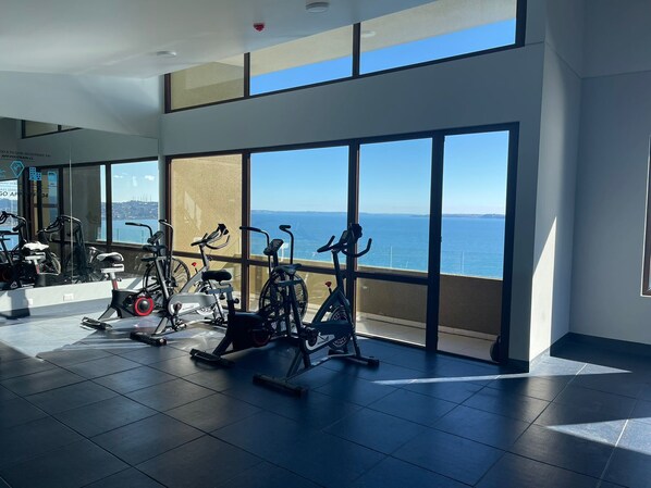 Un gimnasio con equipo de ejercicio y amplias ventanas con vistas al océano.