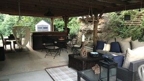 Un espace extérieur aménagé en patio, avec un coin salon couvert, une table, des chaises et un fauteuil suspendu.