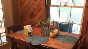 Une table à manger en bois, avec des sets de table verts, des chaises et un vase rempli de fleurs.