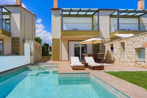 A modern two-story house with a swimming pool, outdoor seating, and stone walls.