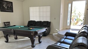 Un salon équipé d’une table de billard, d’un canapé en cuir et d’une porte donnant sur un balcon.