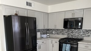 Une cuisine moderne avec des meubles blancs, un réfrigérateur noir, un four à micro-ondes et une cuisinière à gaz.